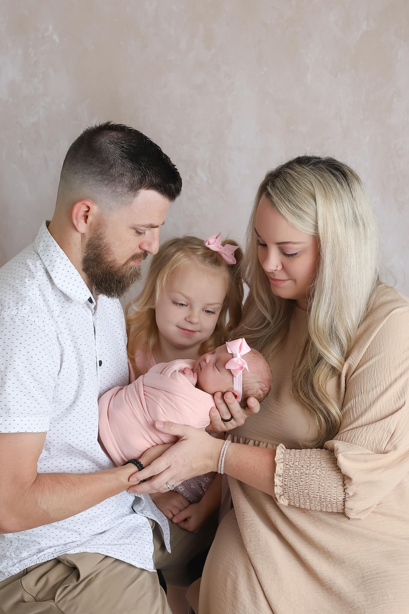 "Kansas City family newborn portrait featuring parents and big sister holding a swaddled baby girl, dressed in soft neutral colors."